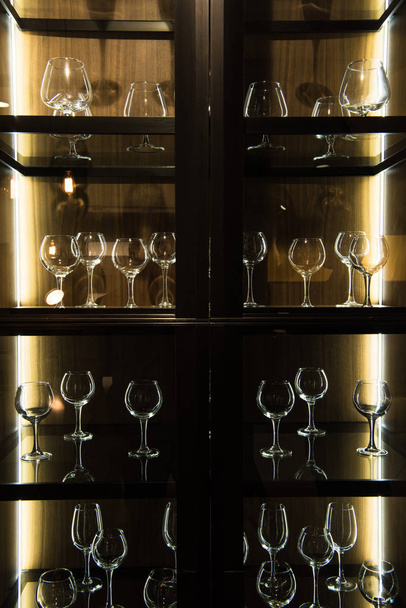 verschillende glazen op de planken in de keuken met donker licht - Foto, afbeelding