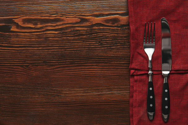 top view of fork and knife on dark red tablecloth on wooden table - Fotó, kép