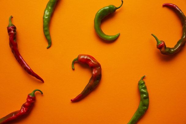 top view of fresh green and red chili peppers on orange background - Fotó, kép