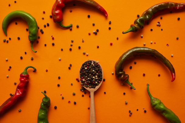 top view of chili peppers and peppercorns in wooden spoon on orange  - Fotó, kép