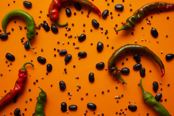top view of chili peppers, haricot beans and peppercorns on orange background - Photo, image