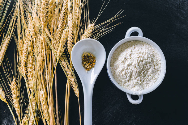Wheat ears and flour on black background, close up - Fotó, kép