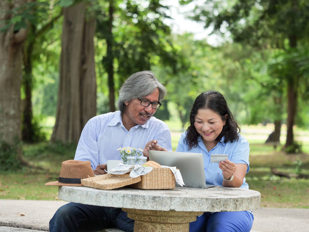 Happy Senior couple picnicking in the garden home.They are using laptop for shopping online together. - Photo, Image