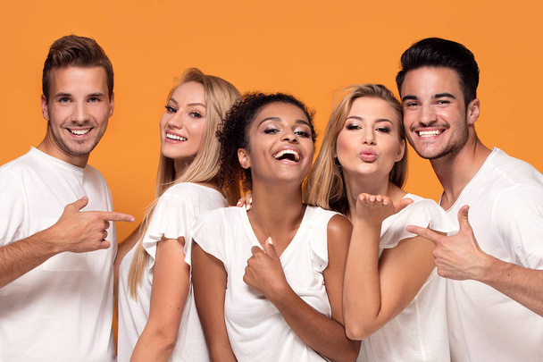 Five young multi ethnic people smiling to the camera, posing on orange studio background in white casual shirts. - Φωτογραφία, εικόνα