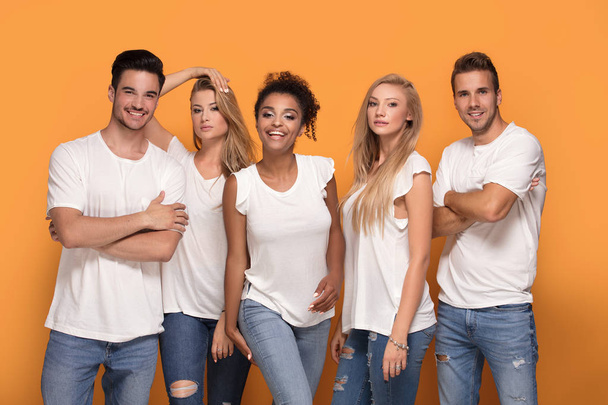 Five young multi ethnic people smiling to the camera, posing on orange studio background in white casual shirts. - Zdjęcie, obraz