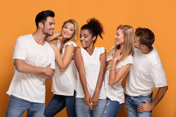 П'ять молодих багатонаціональних людей посміхаються до камери, позуючи на помаранчевому студійному фоні в білих повсякденних сорочках
. - Фото, зображення