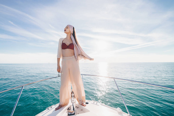 a luxurious girl in stylish summer clothes stands on a yacht in the sun, relaxes and relaxes - Foto, immagini
