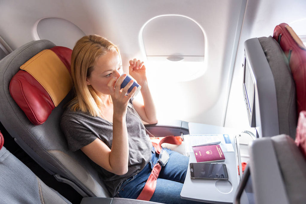 Γυναίκα πίνοντας καφέ σε εμπορική επιβάτες αεροπλάνο κατά την πτήση. - Φωτογραφία, εικόνα