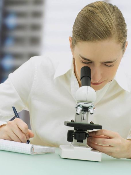 Scientist looking through microscope and writing notes in diary  - Photo, image