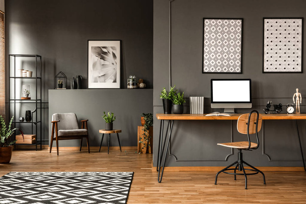 Wooden chair at desk with mockup of computer monitor in grey open space interior with posters - Fotografie, Obrázek