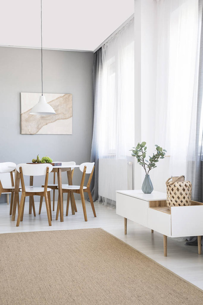White chairs at dining table in scandi flat interior with cupboard, painting and carpet. Real photo - Fotó, kép