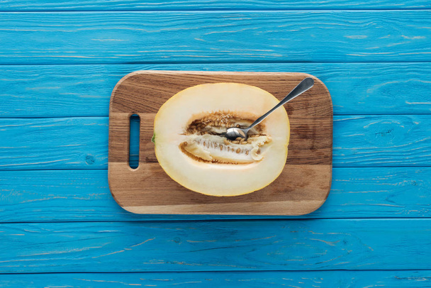 top view of sweet ripe melon with spoon on cutting board on blue wooden surface - Foto, Bild