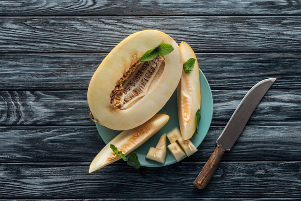 pohled shora sladké zralé plátky melounu s mátou na desku a nůž na dřevěný povrch  - Fotografie, Obrázek
