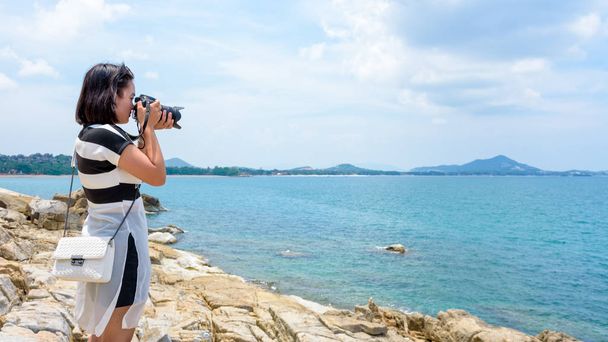 Fiatal nő boldog volt, hogy fotózás dslr fényképezőgép, a rock, közel a tenger alatt a nyári égen a Koh Samui-sziget, Surat Thani tartomány, Thaiföld - Fotó, kép
