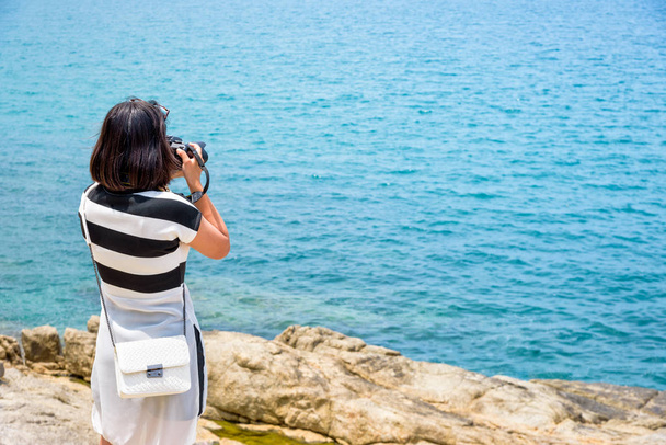 若い女性は、サムイ島、スラタニ県タイで夏空の下で海の近くの岩にデジタル一眼レフ カメラと写真の嬉しかった - 写真・画像