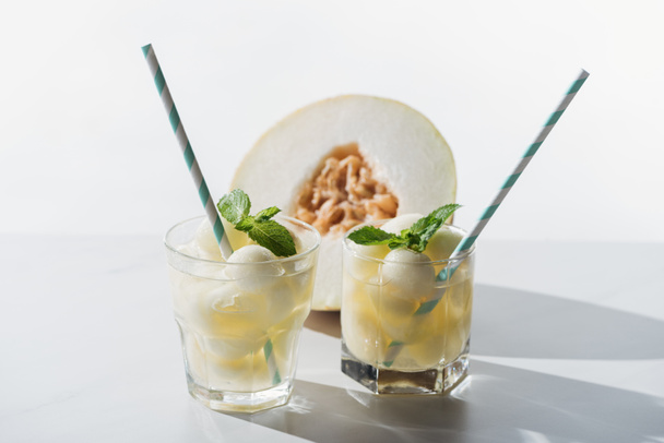 vista close-up de bebida de verão com melão e hortelã em óculos e metade de melão maduro em branco
  - Foto, Imagem