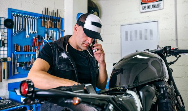 Mecánico hablando de teléfono mientras que la fijación de moto
 - Foto, Imagen