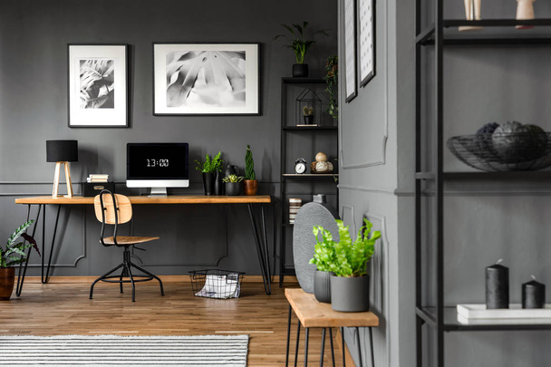 Plants on wooden table in grey home office interior with posters above desk with computer monitor - Foto, Bild