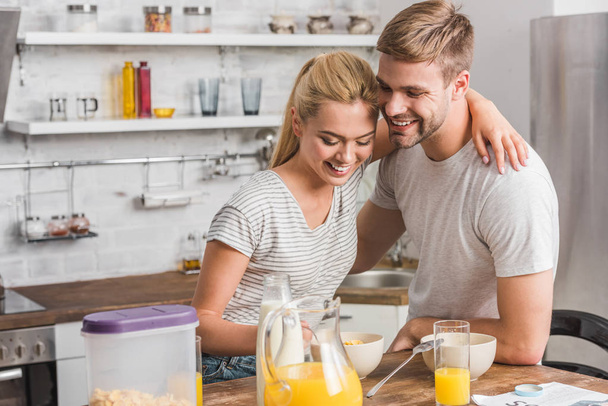 feliz casal sorrindo tomando café da manhã e abraçando na cozinha
 - Foto, Imagem