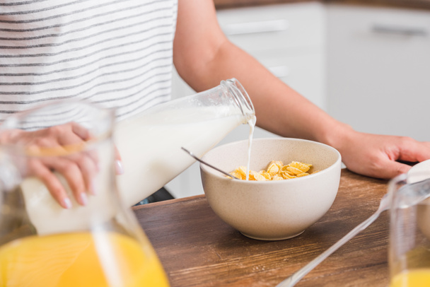 levágott kép lány szakadó tej üveg a lemez kukoricapehely reggeli közben konyha - Fotó, kép