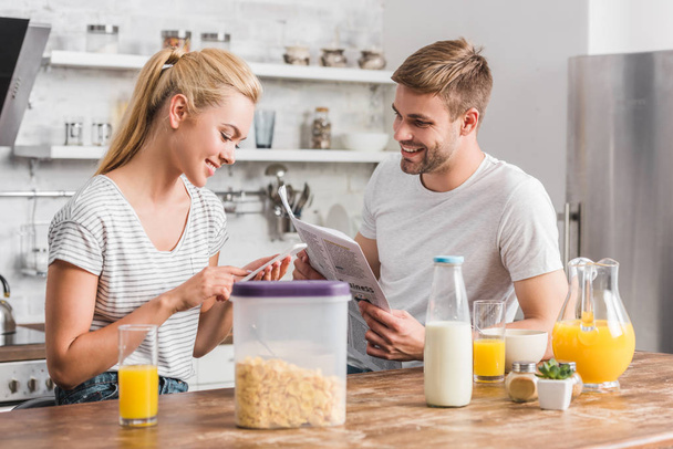 girlfriend using smartphone and boyfriend reading newspaper in kitchen - Foto, immagini