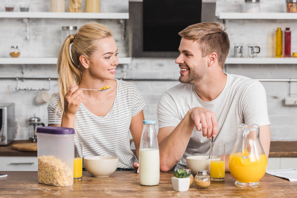 smiling couple having breakfast and looking at each other in kitchen - Foto, Imagen