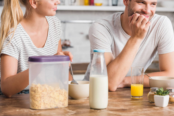 couple having breakfast in kitchen, cornflakes and bottle of milk on table - Fotó, kép