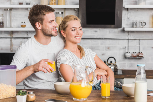 novio feliz abrazando novia durante el desayuno en la cocina y mirando hacia otro lado
 - Foto, Imagen