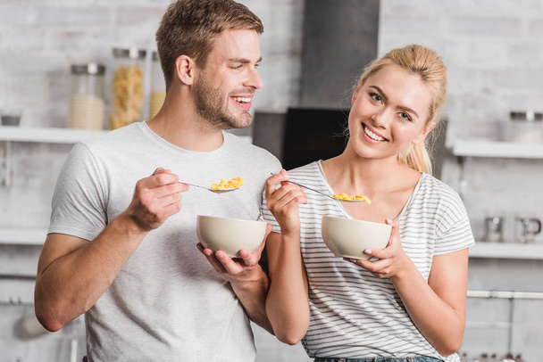 portrait of smiling couple holding plates with corn flakes in kitchen - Fotoğraf, Görsel