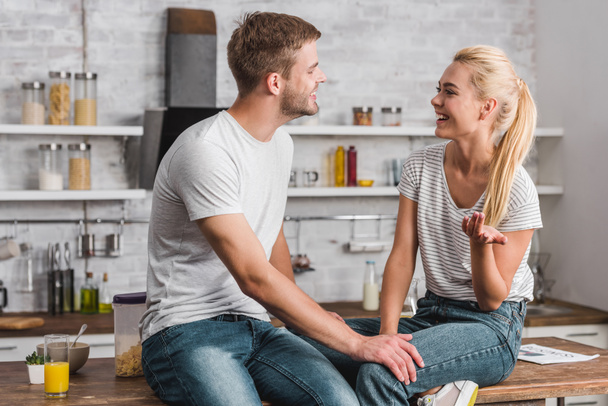 happy couple talking and sitting on kitchen counter - Photo, Image