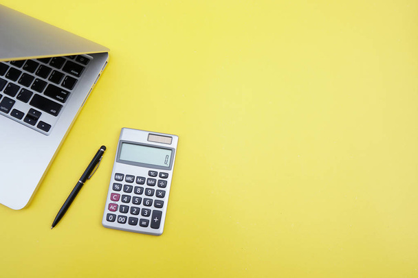 Flat lay, top view office table desk. Workspace with calculator, black pen , laptop on yellow background.Copy Space for text,Empty Blank to word.Business Finance,Education Technology Concept - Φωτογραφία, εικόνα