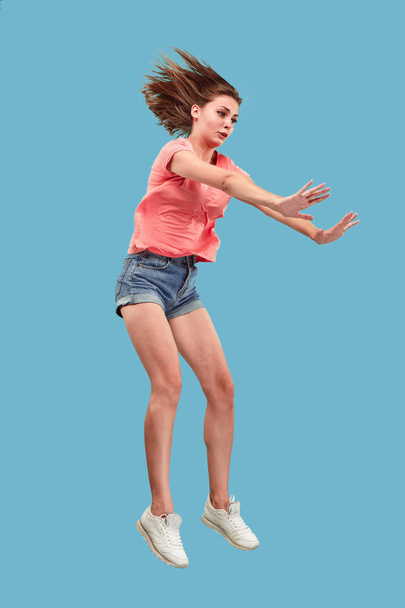 Freedom in moving. Pretty young woman jumping against blue background - Photo, Image
