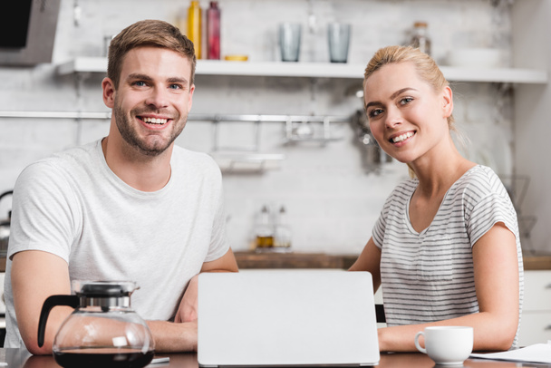 happy young couple using laptop and smiling at camera together  - Φωτογραφία, εικόνα