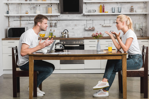 боковой вид эмоциональной молодой пары, ссорящейся во время завтрака на кухне
  - Фото, изображение