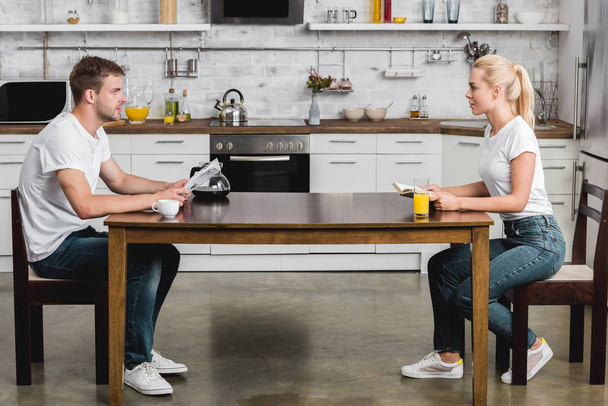 Seitenansicht eines jungen Paares, das einander beim gemeinsamen Frühstück liest und ansieht - Foto, Bild