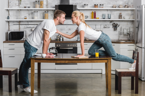 Jong gepassioneerd koppel op zoek naar elkaar, jonge vrouw met t-shirt van knappe vriendje in keuken  - Foto, afbeelding