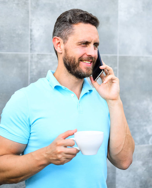 Uomo bere cappuccino parlare telefono grigio muro di sfondo. Il caffè può essere reimmaginato all'infinito fare qualcosa di nuovo vecchio come imprenditori mestiere e reinventare le imprese. Piacevole pausa caffè al lavoro
 - Foto, immagini