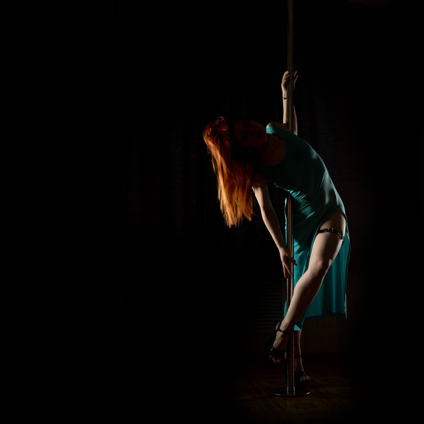 striptease dances with a pole in night club. Gorgeous sexy woman in a long turquoise dress with a slit on a dark background. free space for your text - Φωτογραφία, εικόνα