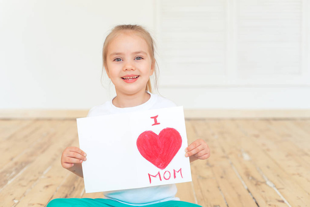 Little girl holding greeting card for Mom on Mothers Day with inscription I love you mom while sitting on floor , Mothers Day concept - Фото, зображення
