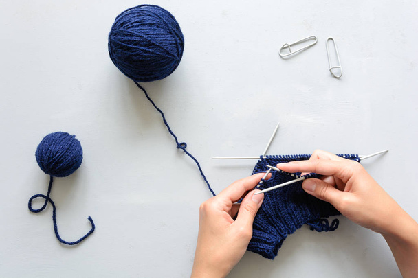 Girl knits blue hat knitting needles on gray wooden background. Process of knitting. Top view. Flat lay - 写真・画像