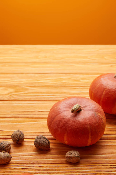 close-up view of ripe orange pumpkins and walnuts on wooden surface - Фото, изображение