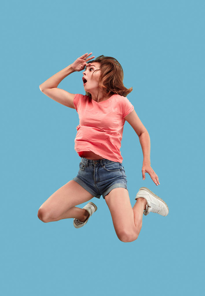 Freedom in moving. Pretty young woman jumping against blue background - Фото, изображение