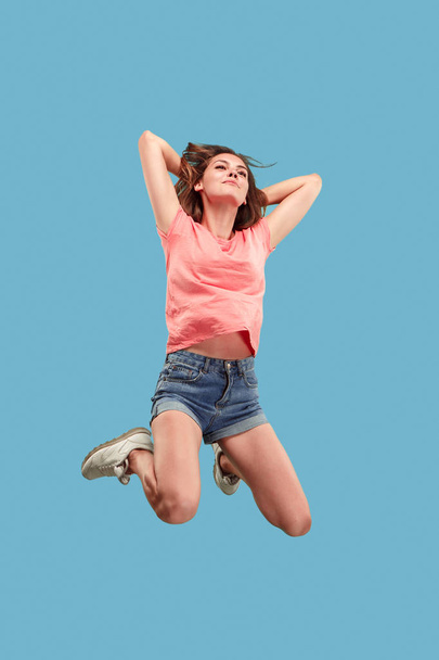 Freedom in moving. Pretty young woman jumping against blue background - Photo, Image