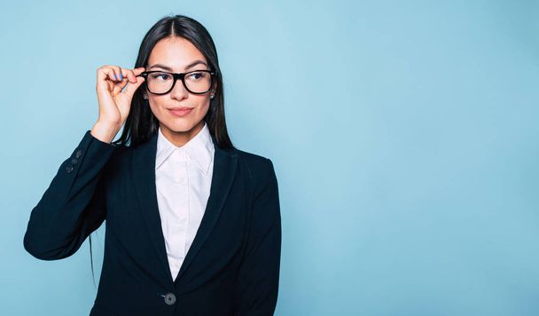 Portrait of young businesswoman fixing glasses on blue background - 写真・画像
