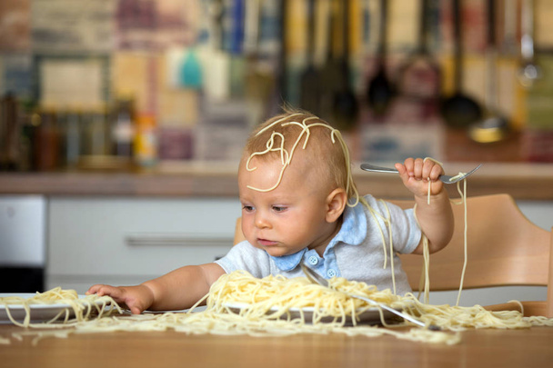 Pikkupoika, taaperolapsi, syö spagettia lounaaksi ja sotkee kotona keittiössä.
 - Valokuva, kuva
