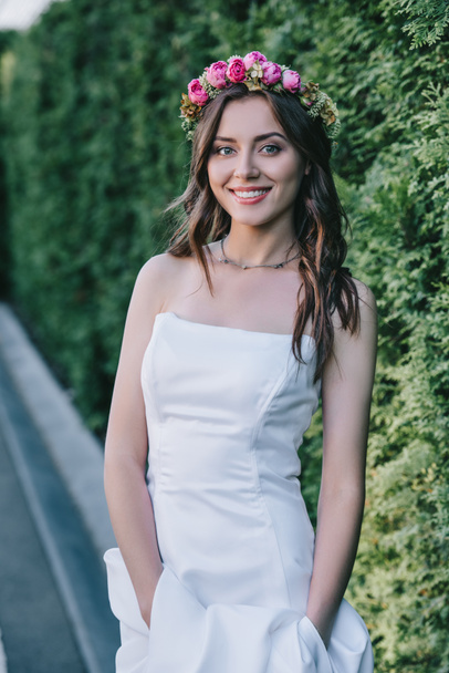 smiling girl posing in traditional white wedding dress and floral wreath - Foto, afbeelding