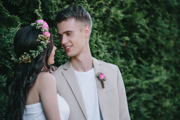 όμορφη νύφη στον floral στεφάνι που βλέπουν happy γαμπρός - Φωτογραφία, εικόνα