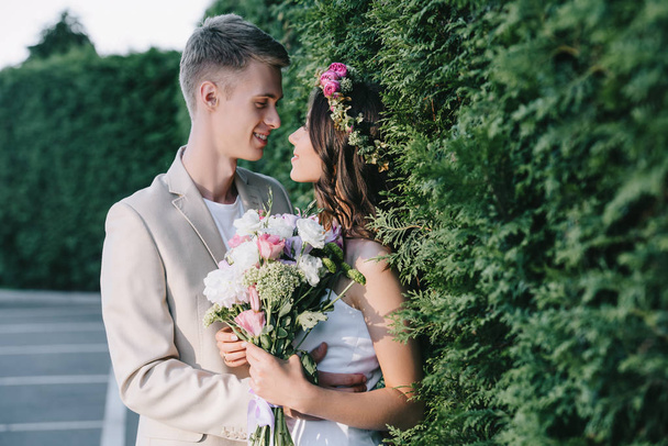 όμορφη γαμήλια ζευγάρι αγκαλιάζει και κρατώντας το παραδοσιακό floral ανθοδέσμη - Φωτογραφία, εικόνα