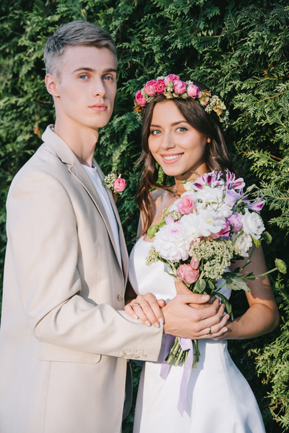 elegant wedding couple with flower bouquet looking at camera - Photo, Image