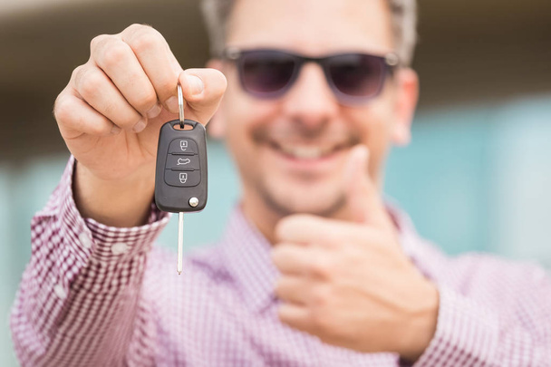 Close up portrait of man holding car key and showing thumbs up. - Фото, изображение